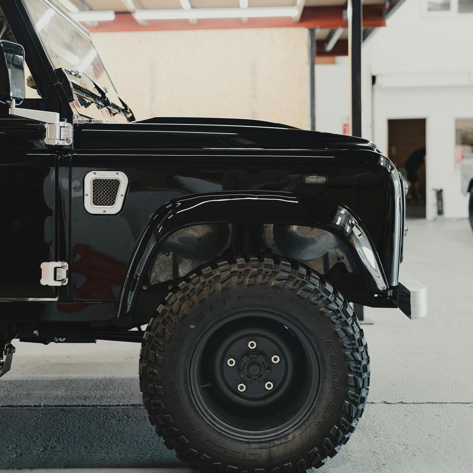 Rugged off-road vehicle wheel with deep tread pattern, mounted on black fender in indoor workshop.