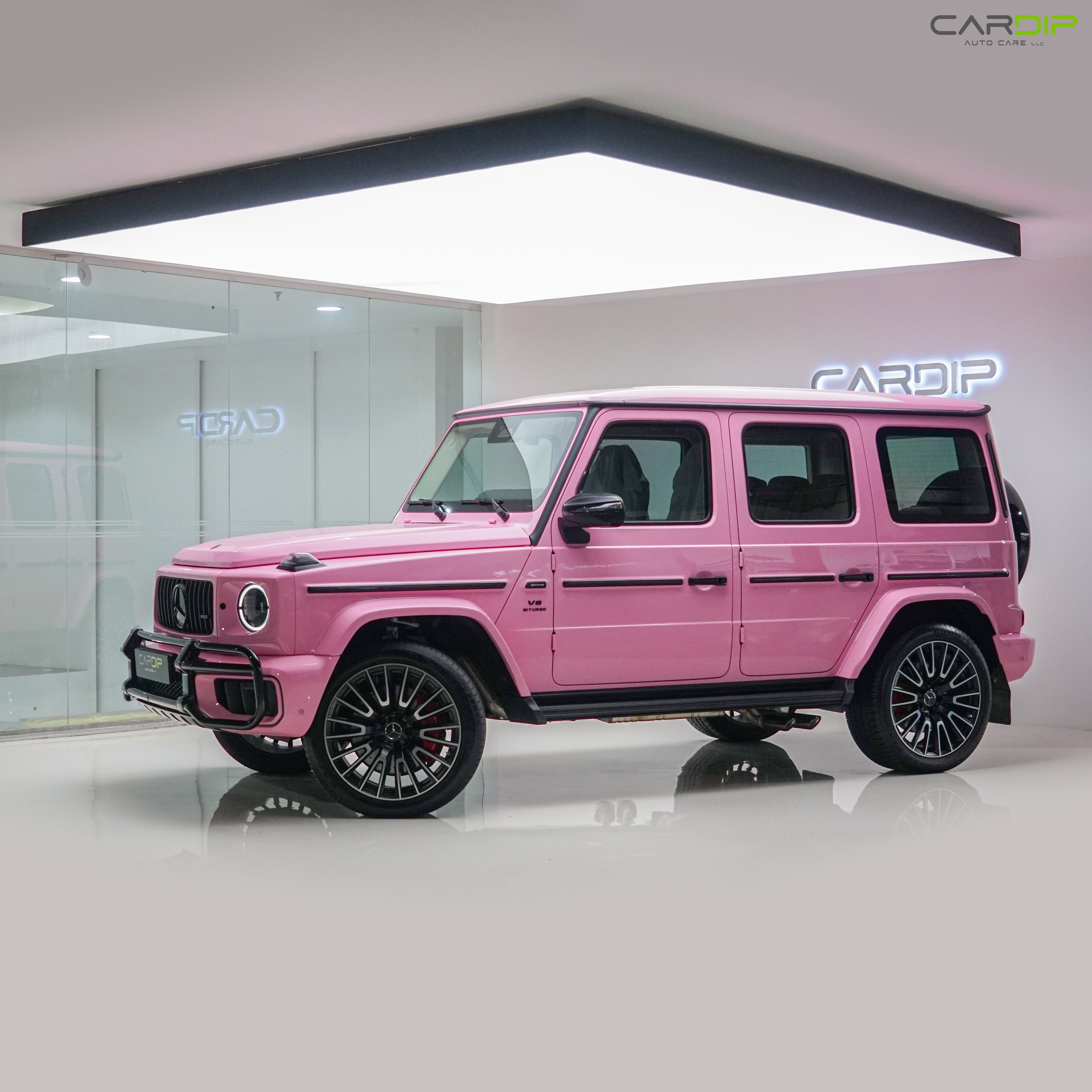 A bright pink Mercedes-Benz G-Class SUV displayed in a modern, well-lit showroom with glossy floors and glass walls.